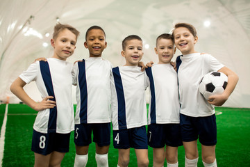 Team of young successful football players in uniform standing in row on field