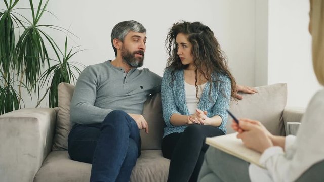Smiling couple listening and talking to professional psychologist and solve relationship porblems during visit psychotherapist office