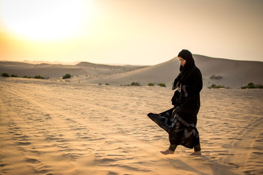 Arabian woman in traditional dress walking through the desert.