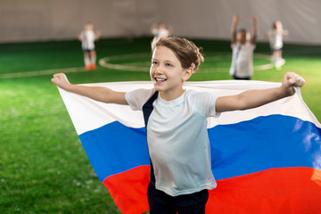Happy youngster outstretching arms with national flag on football field