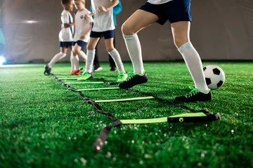 Poster Row of little football players keeping their legs over square cells on green field during training © pressmaster