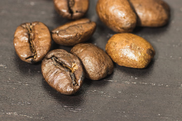 Few dark roasted coffee beans laying on a black table