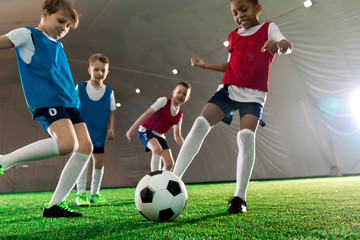 Football team of several little players kicking soccer ball during training