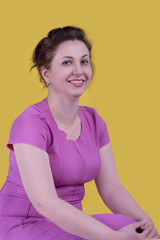 Portrait of the beautiful mature adult woman of the brunette in lilac suit on yellow background.