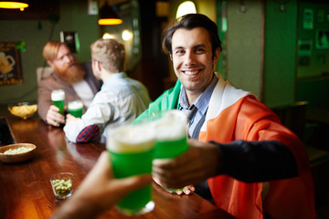 Smiling young man toasting with beer on background of his friends in pub