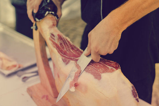 Prosciutto or jamon serrano. Close up on hands of a chef cutting traditional Italian Spanish ham. Slicing prepared hamon gastronomy background