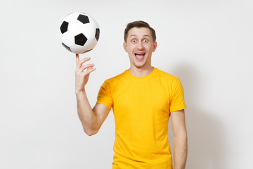 Inspired young cheerful European man, fan or player in yellow uniform spin soccer ball on finger,...