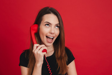 Portrait of chatting woman in black casual having mobile dialog with retro telephone, over red background