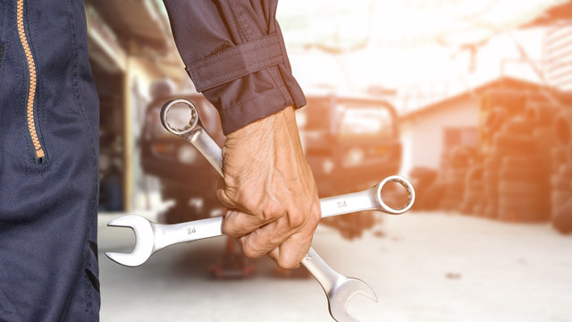 Car repairman wearing a dark blue uniform standing and holding a wrench that is an essential tool for a mechanic and has a backdrop as a car repair center, Automotive industry and garage concepts.