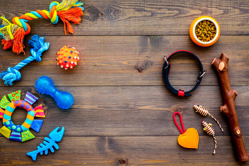 Pet accessories. Toys near bowls with animal feed, collar on dark wooden background top view copy space
