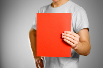 A man in a gray t-shirt keeps a red clean blank sheet of A4. Isolated on grey background