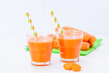 Carrot juice in beautiful glasses, cut orange vegetables and green parsley on white wooden background. Fresh orange drink. Close up photography. Selective focus. Horizontal banner