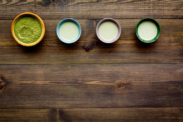 Brew matcha tea. Bowl with powder and cups with beverage on dark wooden background top view copy space