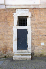 old black metal iron door with white stone marble frame portal in red brick wall