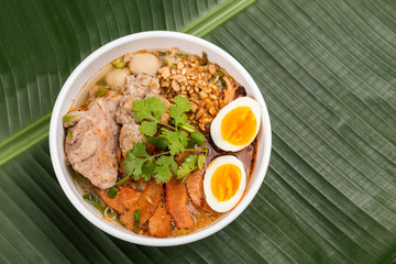 Spicy noodle soup with pork and egg in bowl on banana leaf