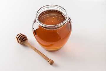 Honey dipper and honey in jar on white background.
