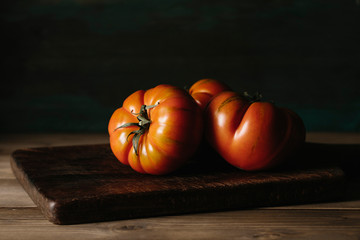 Delicious red raf tomatoes on a wooden table on a dark background. - obrazy, fototapety, plakaty