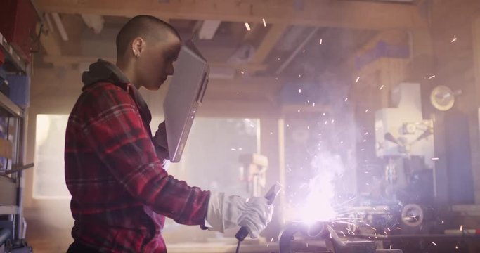 Portrait of young powerful woman welding in workshop