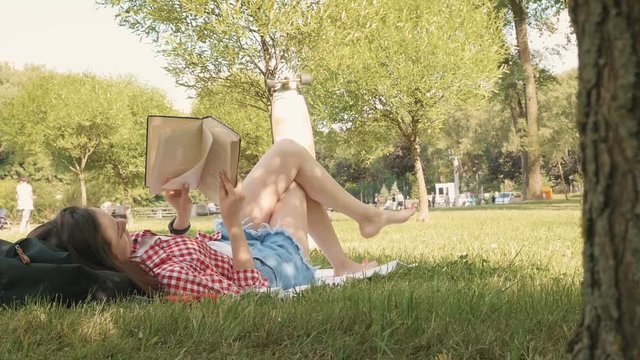 Woman lay down or relaxing on green grass reading book in summer or spring