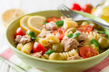 Fusilli pasta salad with tuna, tomatoes, olives and parsley on white wooden background.