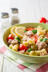Fusilli pasta salad with tuna, tomatoes, olives and parsley on white wooden background.