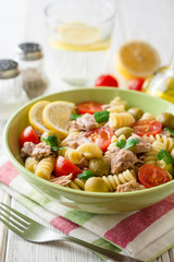 Fusilli pasta salad with tuna, tomatoes, olives and parsley on white wooden background.