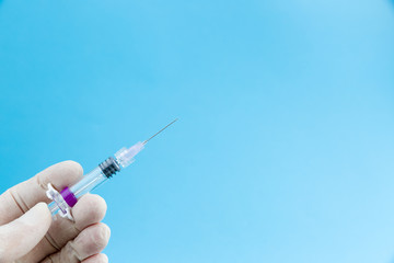 Syringe needle with influenza vaccine or medicine in doctors hands in white medical gloves isolated on blue background copy space