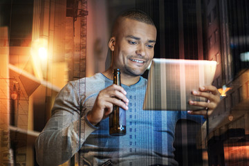 Leisure time. Happy young smiling man having a good time while watching films on his modern tablet and drinking beer
