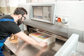 Worker in uniform lining up a stack of paper in the cutting machine at the manufacturing