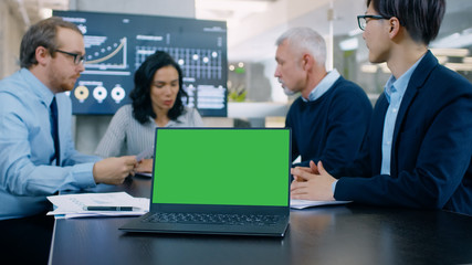 In the Meeting Room Laptop with Green Chroma Key Screen on the Conference Table. In the Background Business People Have Important Discussion.