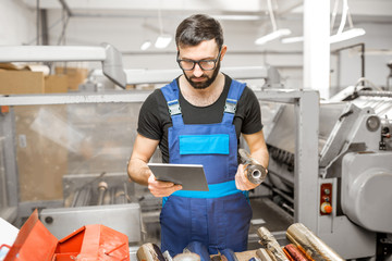 Handsome worker holding cliche and foil roll for stamping standing at the vintage printing manufacturing