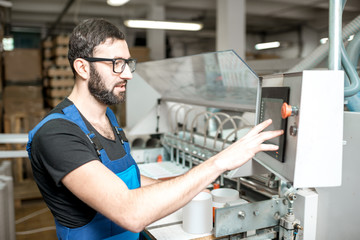 Man in uniform working with machine that makes paper tubes at the printing manufacturing