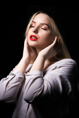 Tender blonde woman wearing white blouse, posing in the dark at studio