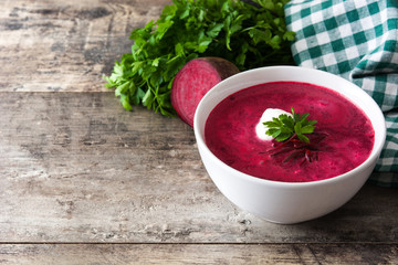 Beet soup in white bowl on wooden table. Copyspace