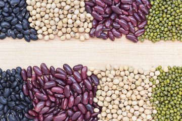 A pile of many types of beans divided into two rows on the wood table.