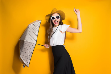 beautiful happy young woman in fashion hat and sunglasses posing on yellow background holding an...