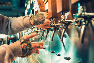 Hand of bartender pouring a large lager beer in tap.