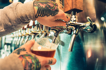 Hand of bartender pouring a large lager beer in tap.