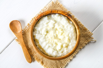 Rice milk porridge with nuts and raisins in wooden bowls on a white wooden table.