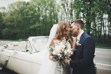 Stylish wedding couple, bride, groom kissing and hugging on retro car