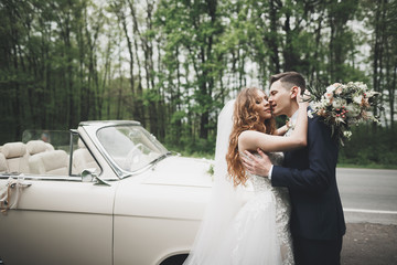Stylish wedding couple, bride, groom kissing and hugging on retro car