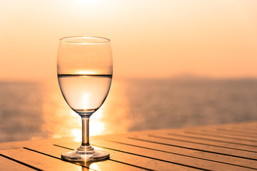 Silhouette glass of wine on a wooden table with  seascape and skyline in the evening with sunset tone style.