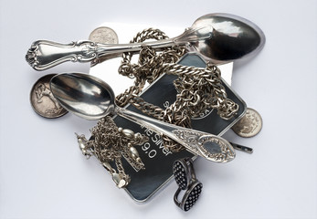 Silver ware are placed on a light gray background. Silver bars, old coins, a teaspoon, a coffee...