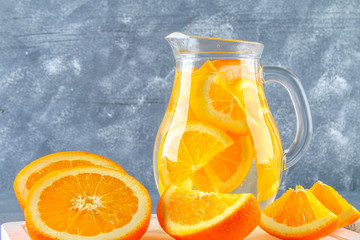Orange detox water in a pitcher on a gray concrete background. Healthy food, drinks.