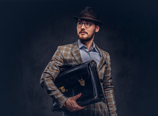 A bearded man wearing casual suit in a hat and glasses holds sui
