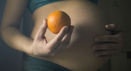 Pregnant woman holding Orange fruit at her tummy.