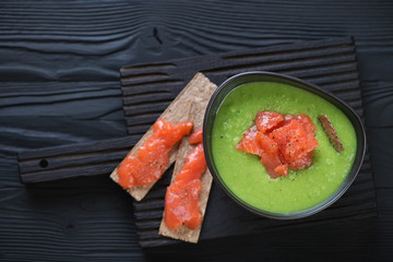 Cream-soup with green peas topped with salmon fillet, view from above on a black wooden background, studio shot