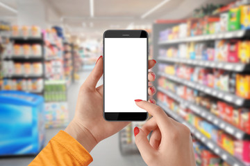 Fototapeta na wymiar Woman use mobile phone with blank screen, blurred supermarket in background