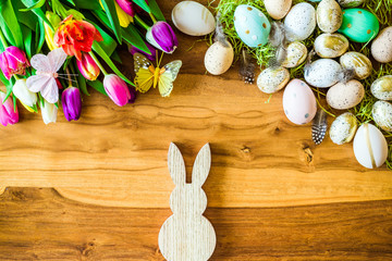 Fototapeta Freifläche auf Holztisch im Hintergrund und Osterdekoration wie bunte verzierte Ostereier, Federn, Schmetterlinge und Tulpen von oben zu Ostern obraz