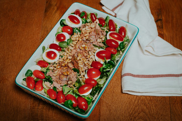 green salad with tuna, egg, tomatoes, roasted pine nuts, Charlotten, vinegar and oil on wooden...
